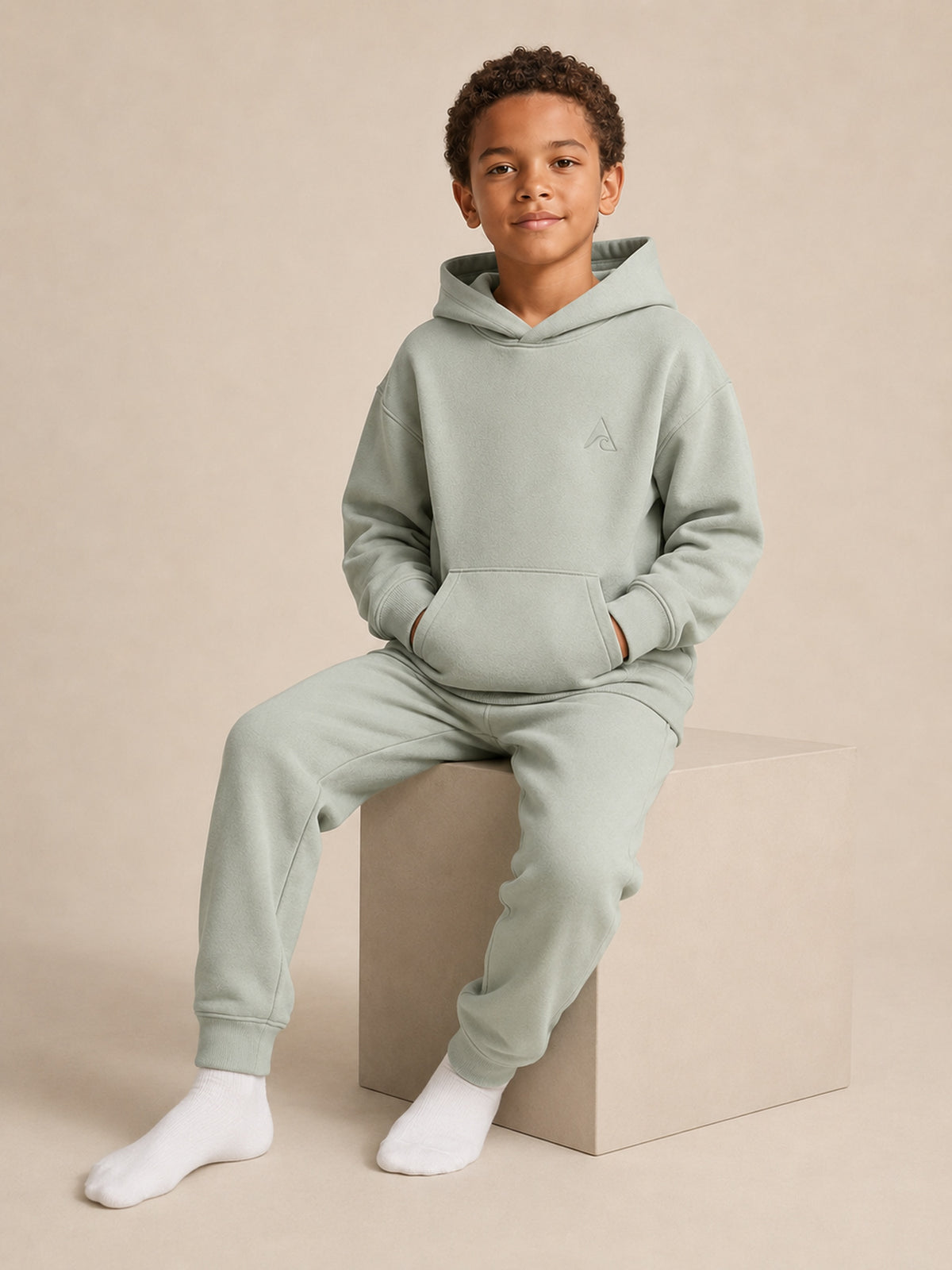 Akumi Little Driftlight Hoodie in Cloud Sage seated studio pose