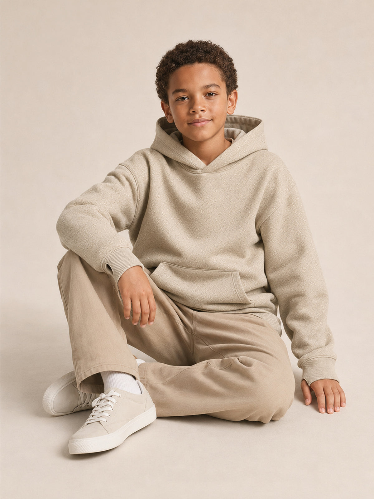 Akumi Little Fieldstitch Kids Hoodie in Oat Meadow seated studio pose