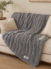 Akumi Warmline Blanket draped across sofa in Mica Grey with controller and woven label